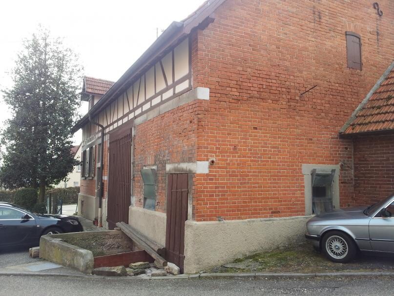 Rotbraunes Backsteingebäude mit Fachwerk-Elementen, Türen, Fenster und geparktes Auto rechts.