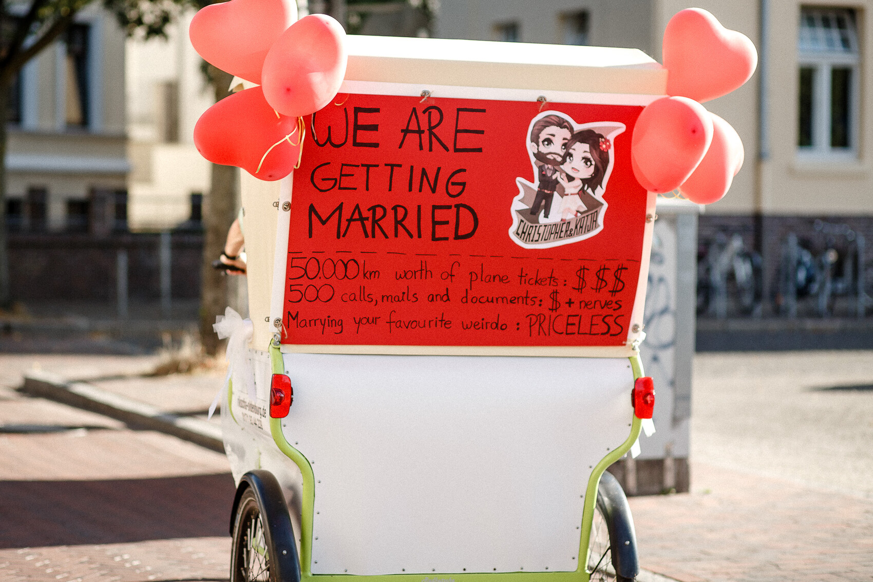 Rot beschilderter Wagen mit pinken Herzballons, Schild "We are getting married".