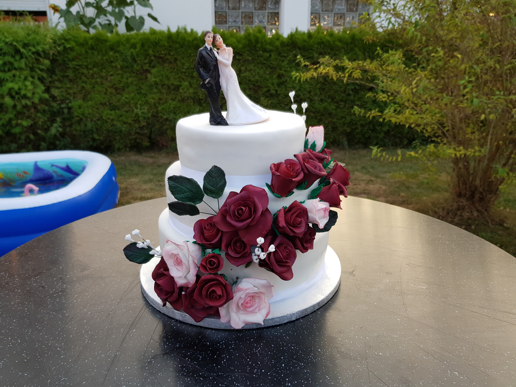 Dreistöckige Hochzeitstorte mit roten Rosen und Brautpaar-Figur auf der Spitze.