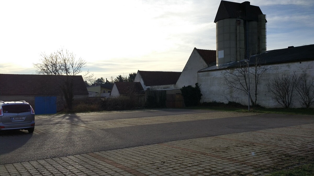 Außenansicht eines Hofgeländes mit Scheune, Silos, Gebäuden und geparktem Auto.