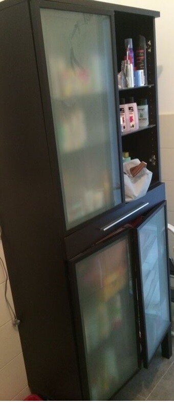 Dunkler Badschrank mit zwei milchglasigen Türen und offenen Regalfächern.