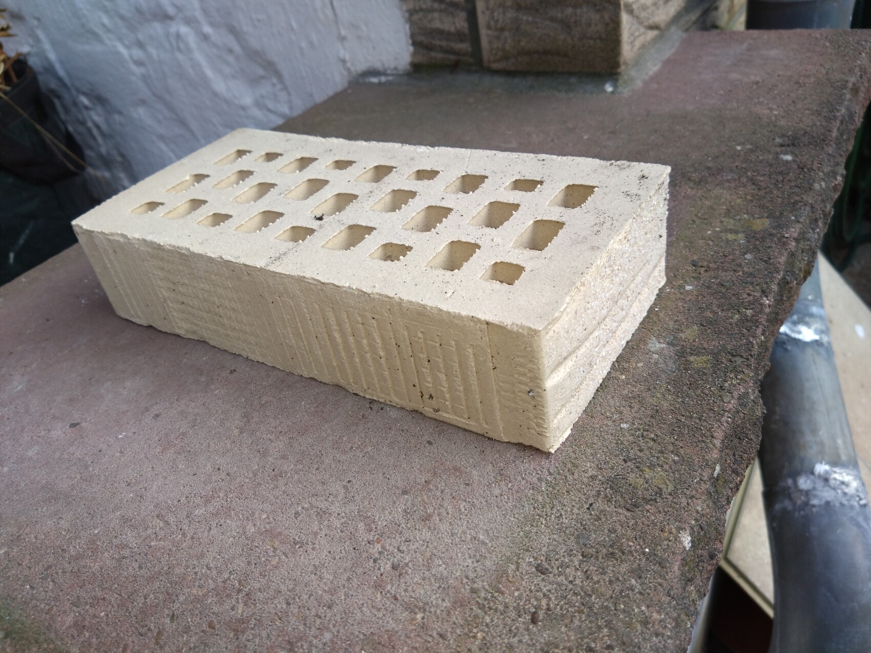 Beiger Hohlblock mit ovalen Öffnungen liegt auf Steinplatte im Freien