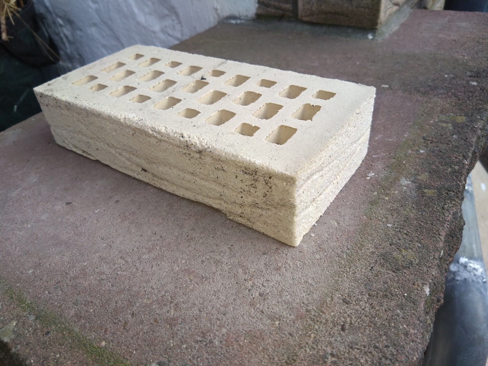 Hellbeiger Betonblock mit mehreren rechteckigen Öffnungen liegt auf rauer Steinoberfläche im Freien.