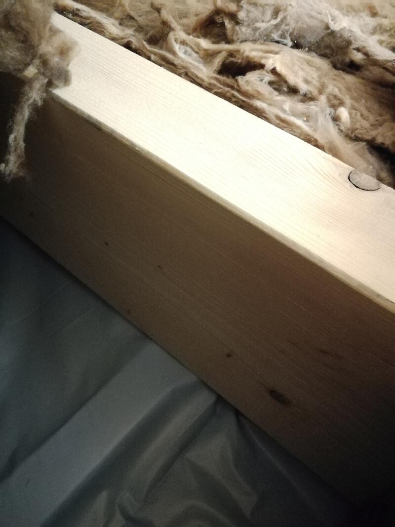 Holzlatte mit Dämmwolle oben; darunter graue Folie.