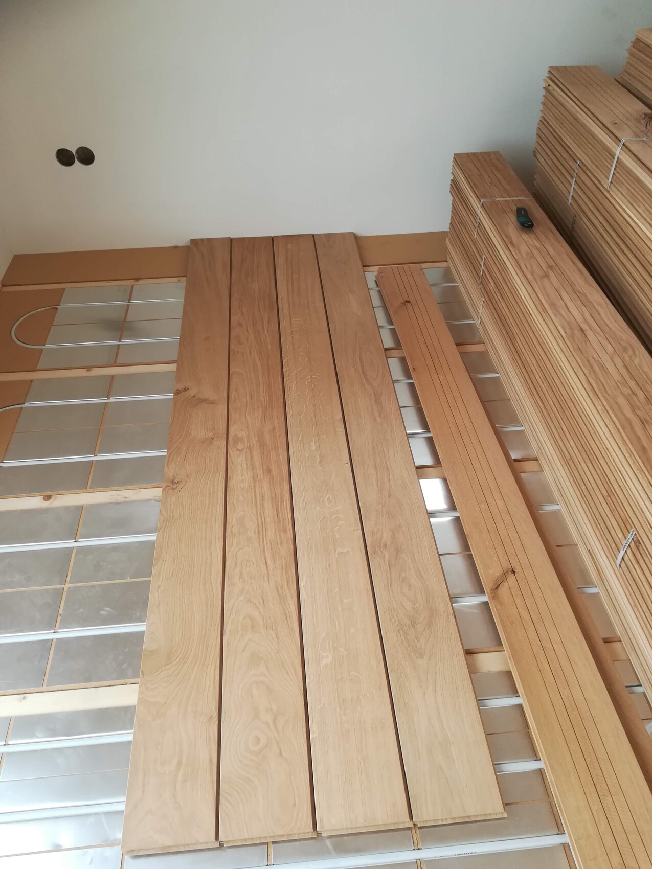 Holzbretter liegen auf einem Metallrahmen; rechts stapeln sich Bretter, ein Werkzeug liegt darauf.