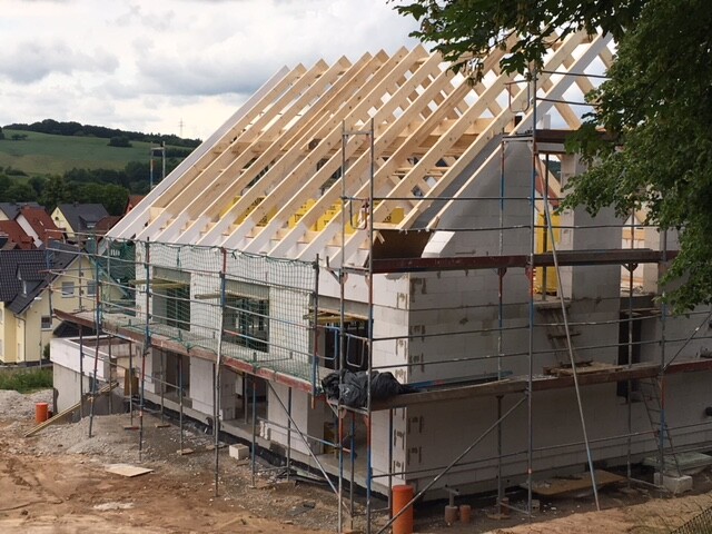 Rohbau eines Hauses mit sichtbarem Holz-Dachstuhl, Gerüst rundum auf der Baustelle.