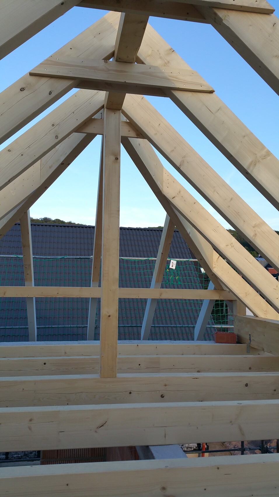 Holz-Dachstuhl mit Sparren, Mittelpfeiler und Holzbalken; Blick durch Rohbau zum blauen Himmel