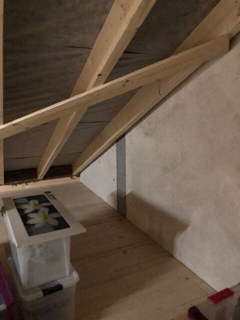Dachboden mit Holzbalken, Kunststoffboxen und einem Bilderrahmen mit weißen Blumen.