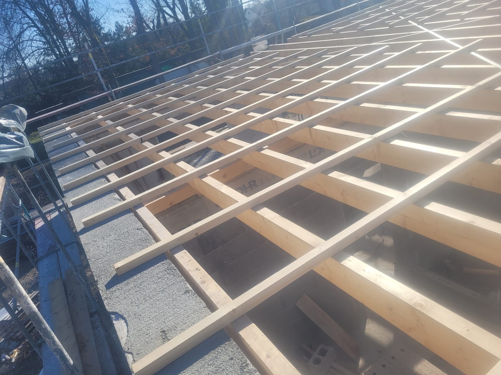 Holz-Dachkonstruktion aus Balken und Latten über einem Gebäude; Baugerüst links sichtbar
