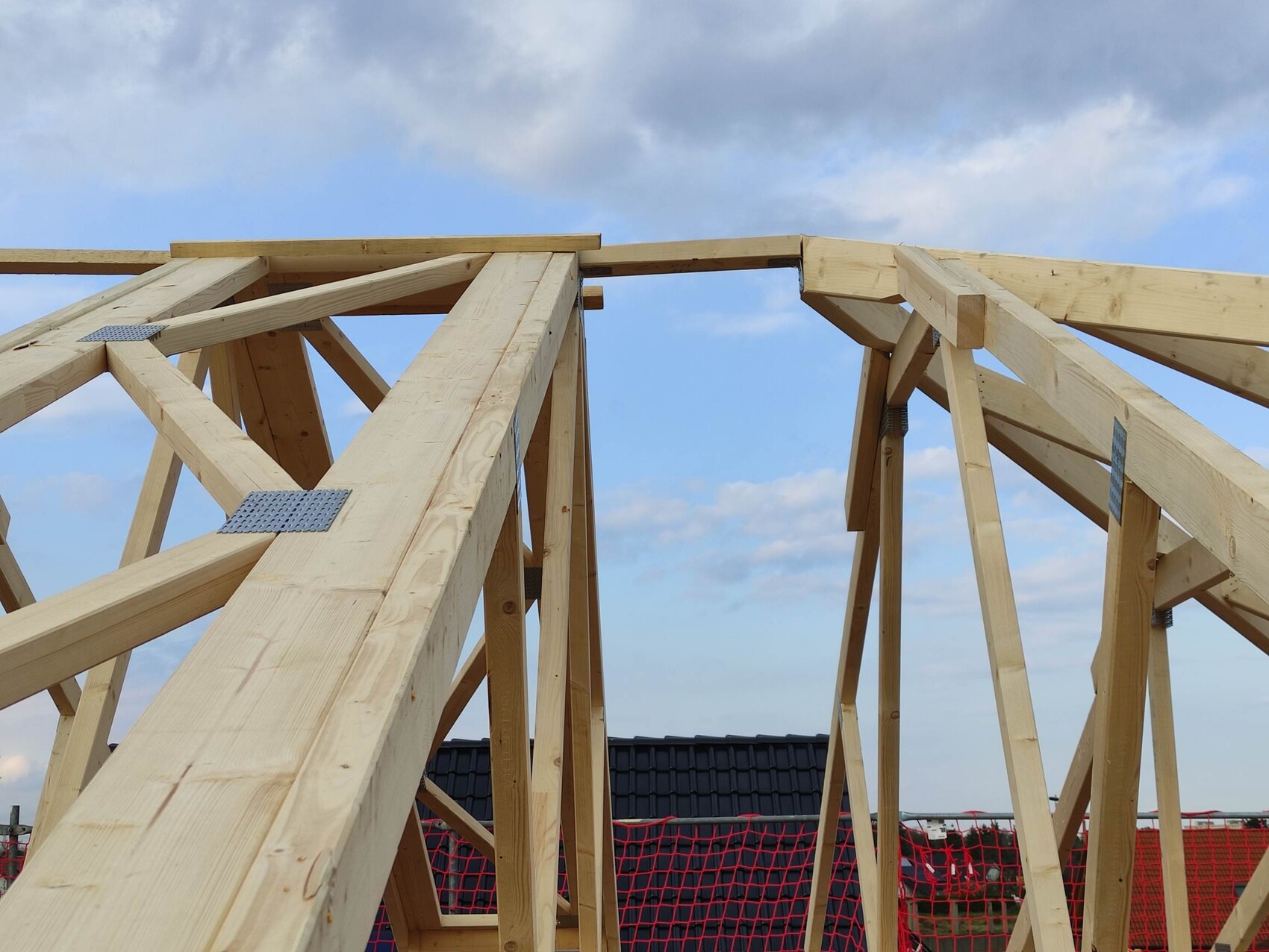 Holz-Dachkonstruktion mit Balken und Metallverbindern im Rohbau gegen blauen Himmel