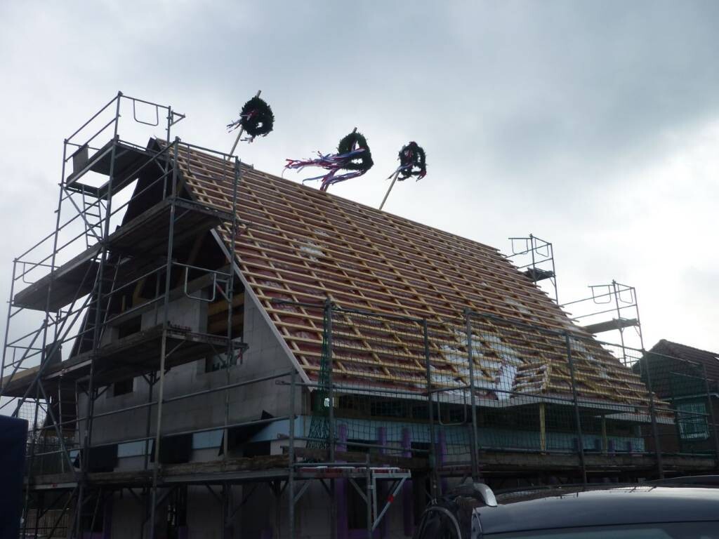 Hausbau im Rohbau mit Gerüst; Dach wird gedeckt, Kränze auf dem Dach.