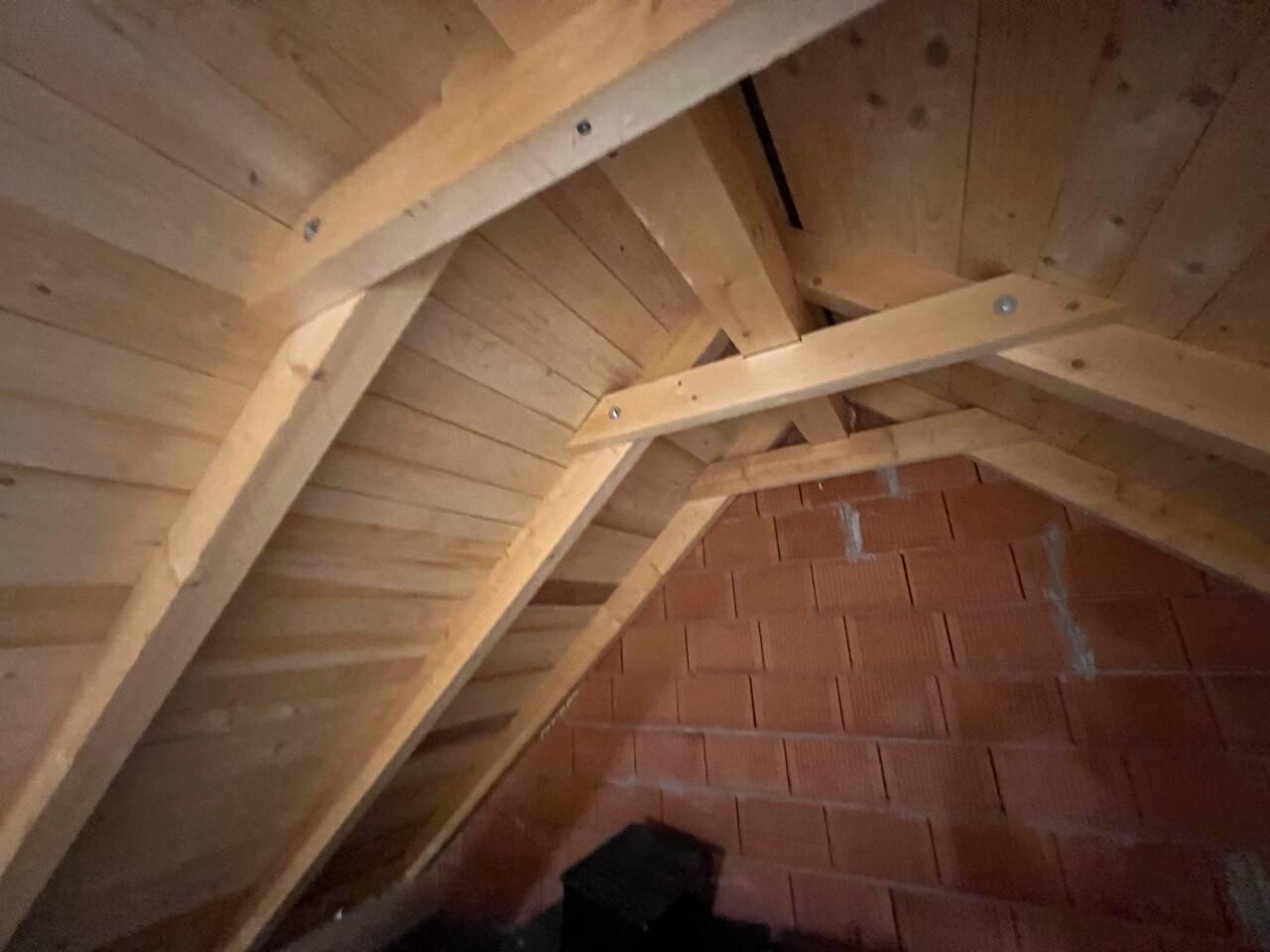 Unfertiger Dachboden mit sichtbarem Holzdachstuhl und roter Ziegelwand