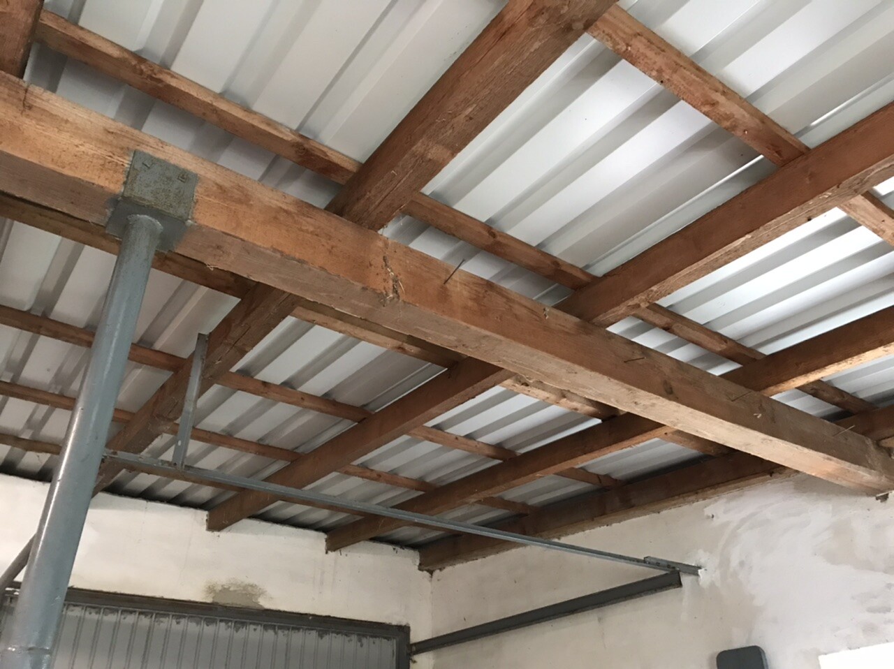 Sichtbare Holzbalkendecke mit Stahlstütze und Wellblech-Dach im Innenraum