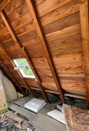 Holz-Dachstuhl im unbeheizten Dachboden mit Dachfenster und Baumaterialien