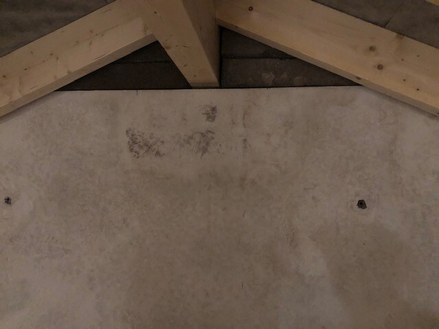 Dachgeschoss mit sichtbaren Holz-Balken und rauer Beton-/Putzwand im Hintergrund.