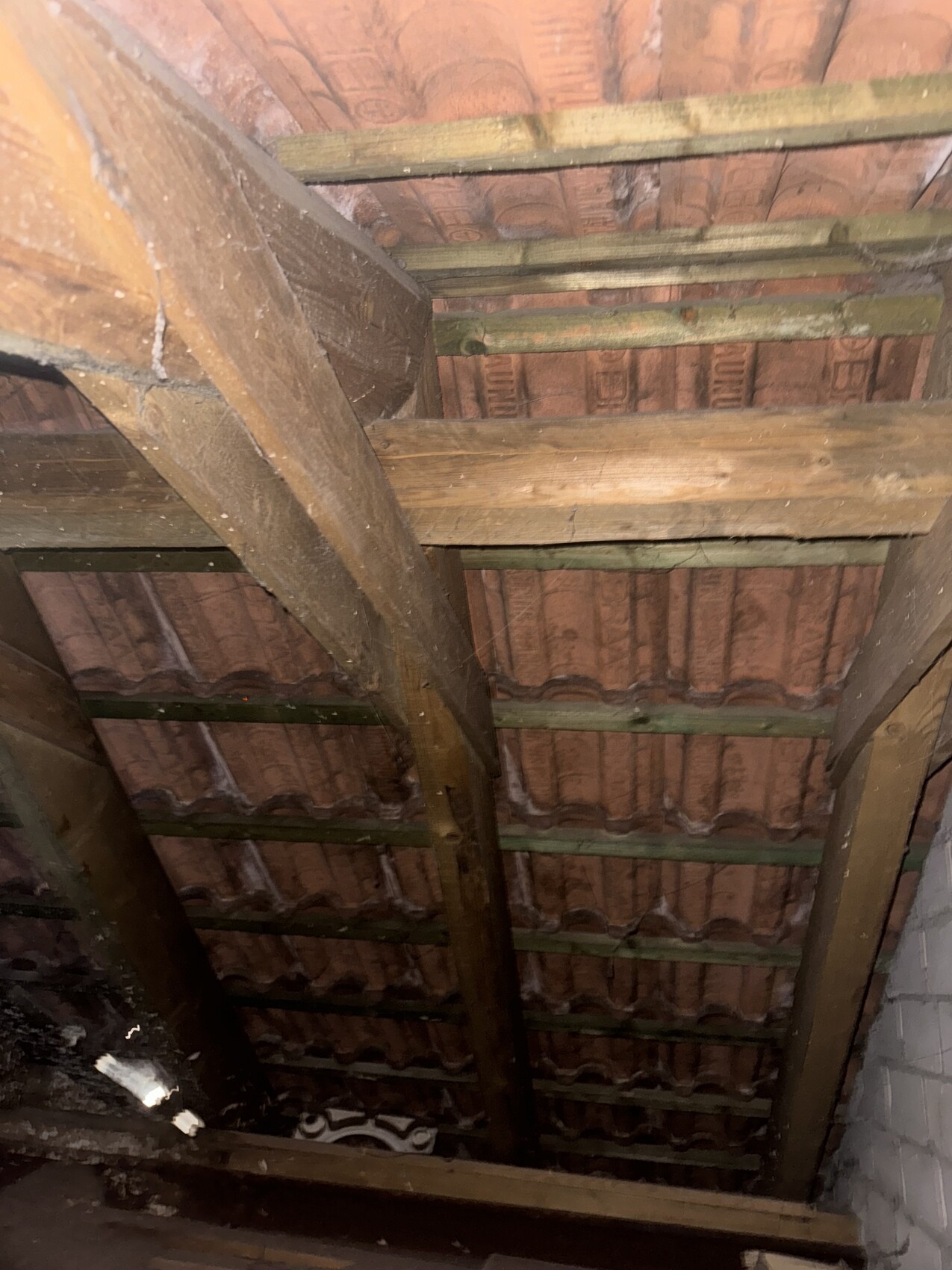 Dachboden mit Holzbalken und rotem Ziegeldach, dunkle Ecke.