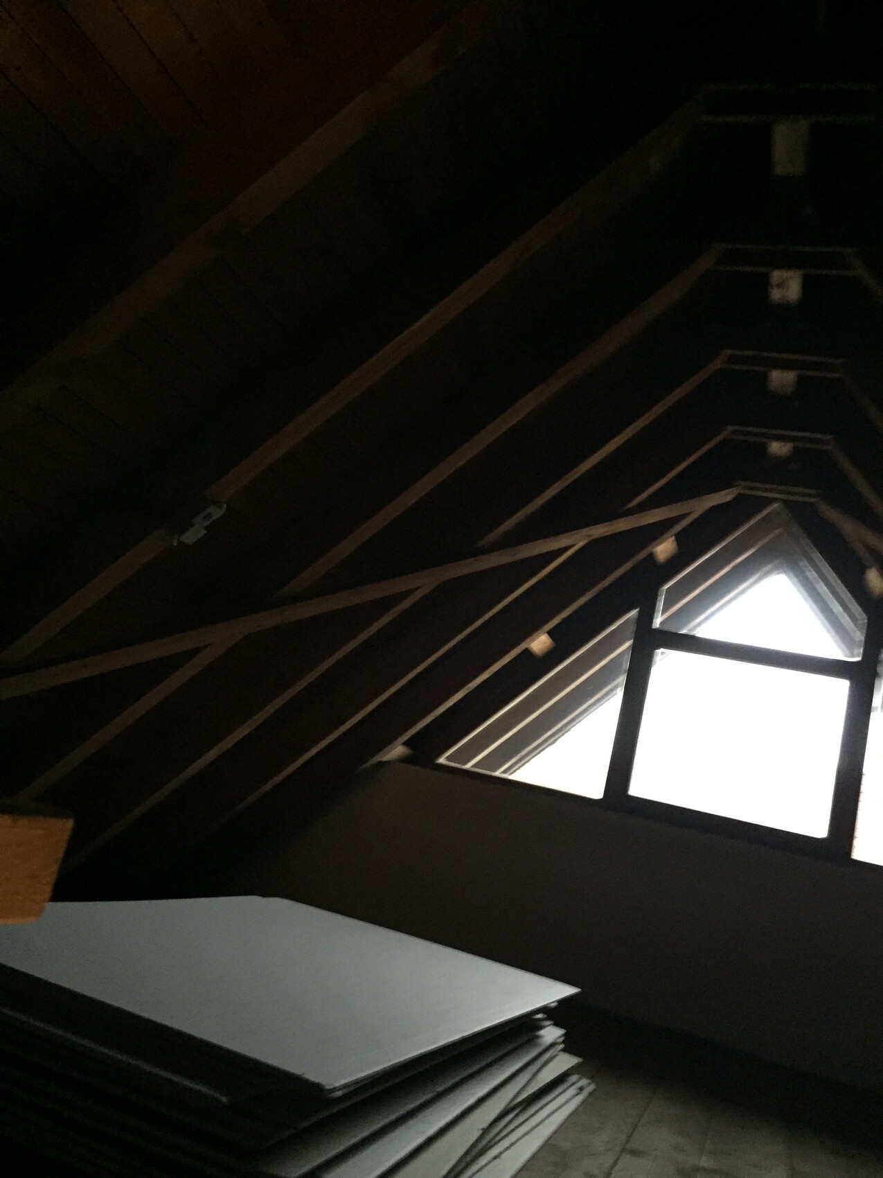 Dachboden mit Holzbalken, schrägem Dachfenster und gestapelten Platten am Boden.