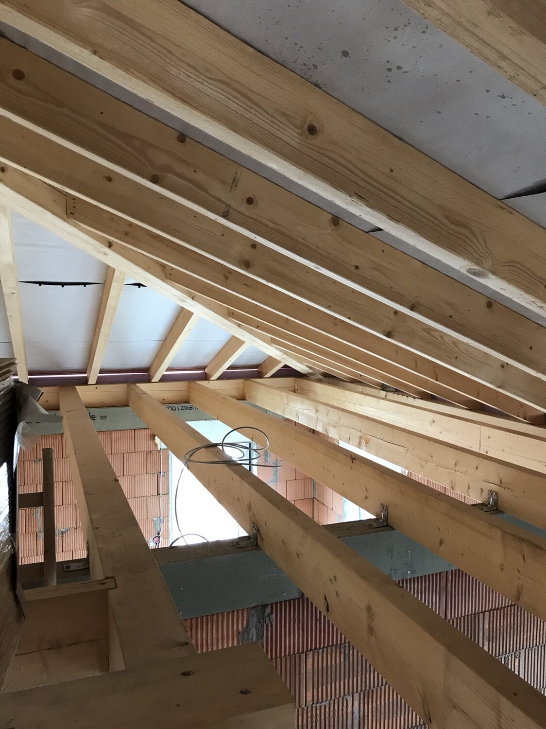 Rohbau: Dachstuhl aus Holz mit Sparren, freiliegende Kabel, rote Ziegelwände.