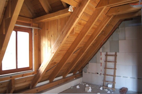 Holz-Dachstuhl im Rohbau mit Fenster links, Leiter und losem Baustoff am Boden