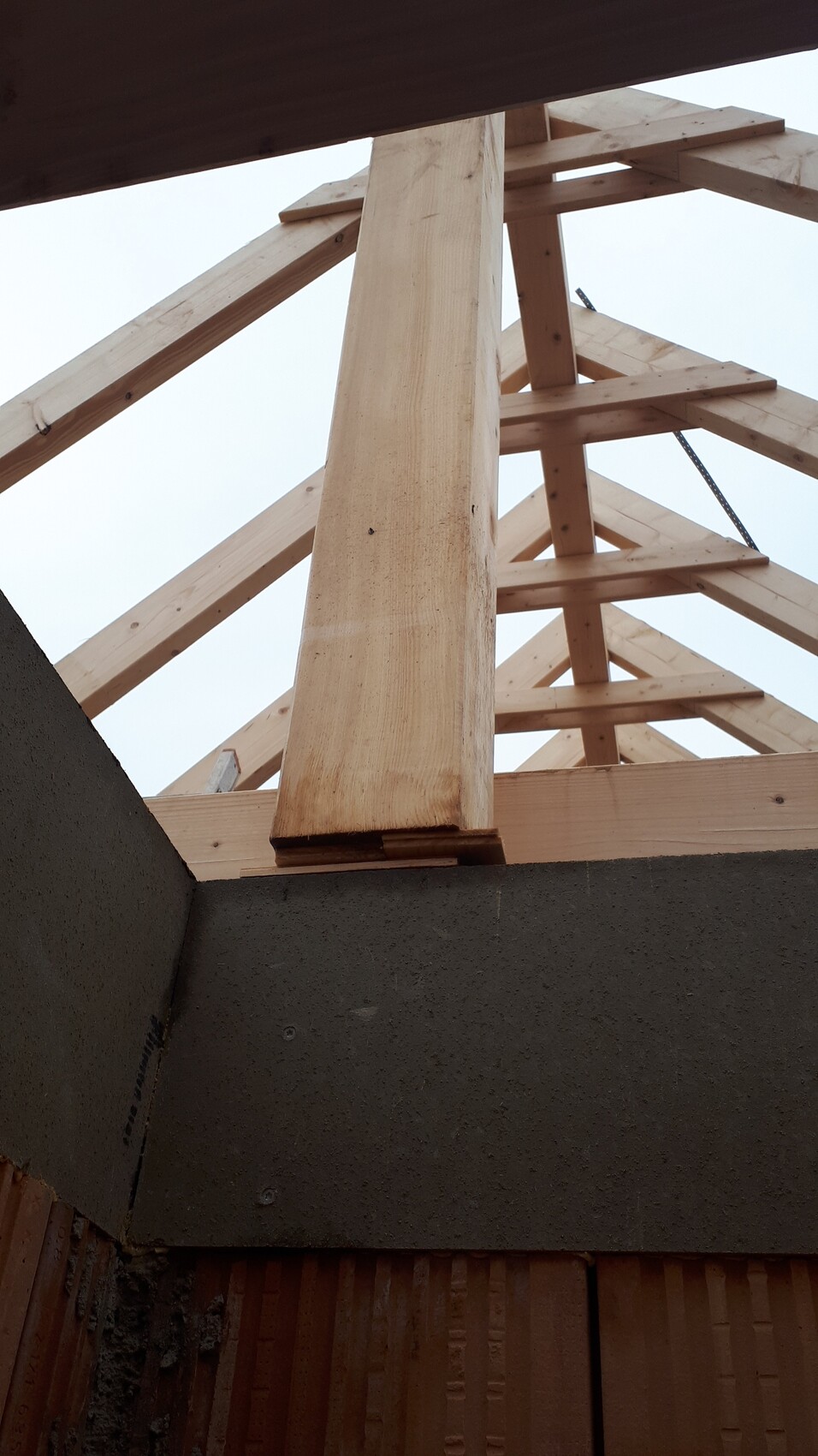Holz-Dachstuhlrahmen eines Neubaus, tragende Balken über Rohbauwand, Blick nach oben.