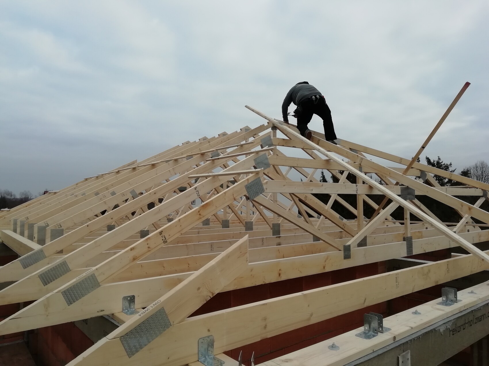 Mitarbeiter montiert Holzdachstuhl auf einem Rohbau unter wolkigem Himmel.