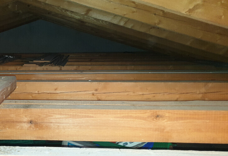 Dachboden mit sichtbaren Holzbalken, Dachlatten und gelagertem Material.