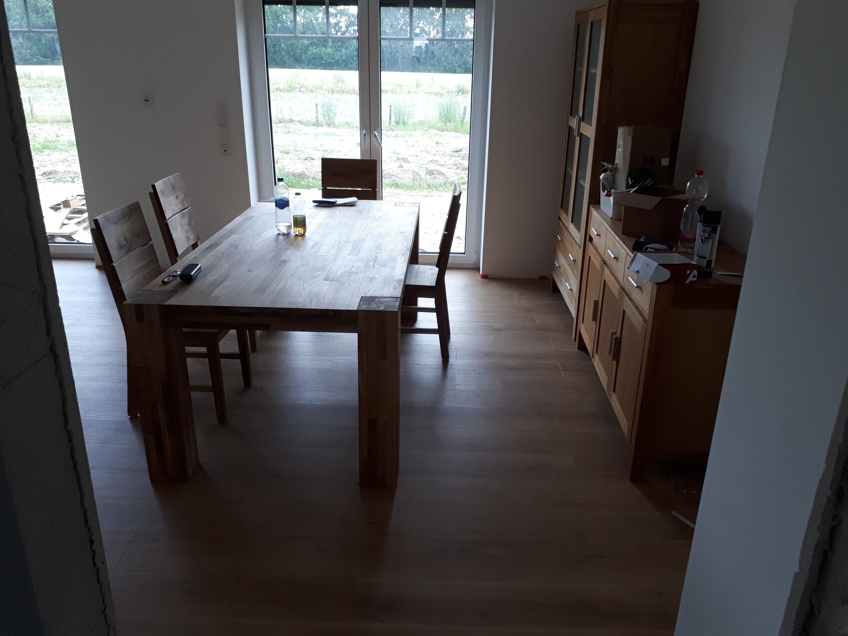 Helles Esszimmer mit massivem Holztisch und Stühlen, Glas-Tür zum Garten; rechts ein Holzsideboard.