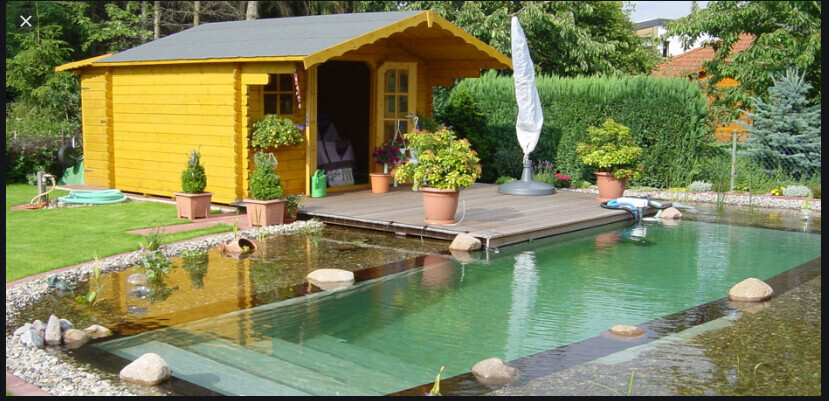 Gelb gestrichenes Gartenhaus auf Holzdeck neben klarem Garten-Teich-Pool, von Pflanzen umgeben