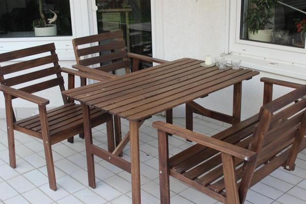 Holz-Gartenmobel Esstisch mit vier Stuehlen auf heller Terrassenfliese vor Haus