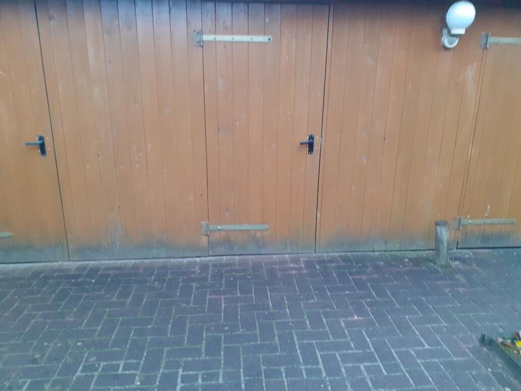 Braune Holztüren mit schwarzen Griffen und Metallbeschlägen vor dunklem Pflaster.