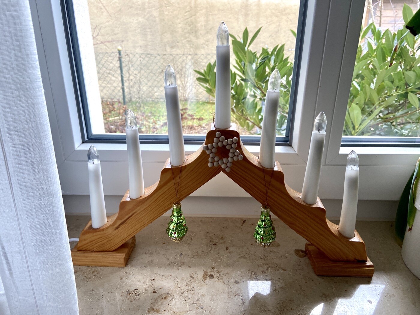Holz-Kandelaber mit weißen Kerzen und grünen Glaskugeln vor dem Fenster.