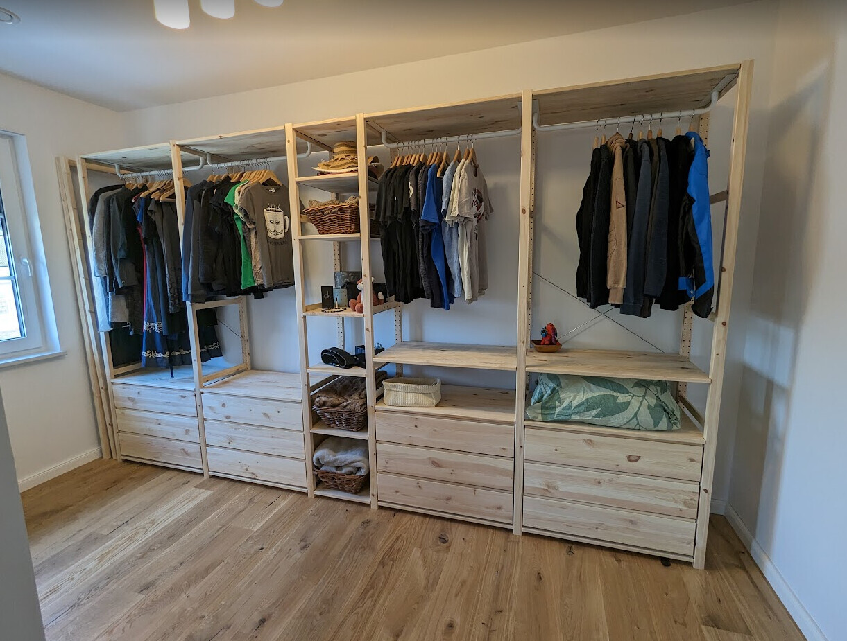 Offenes Holz-Kleidersystem mit Hängestangen, Schubladen und Körben im Zimmer.