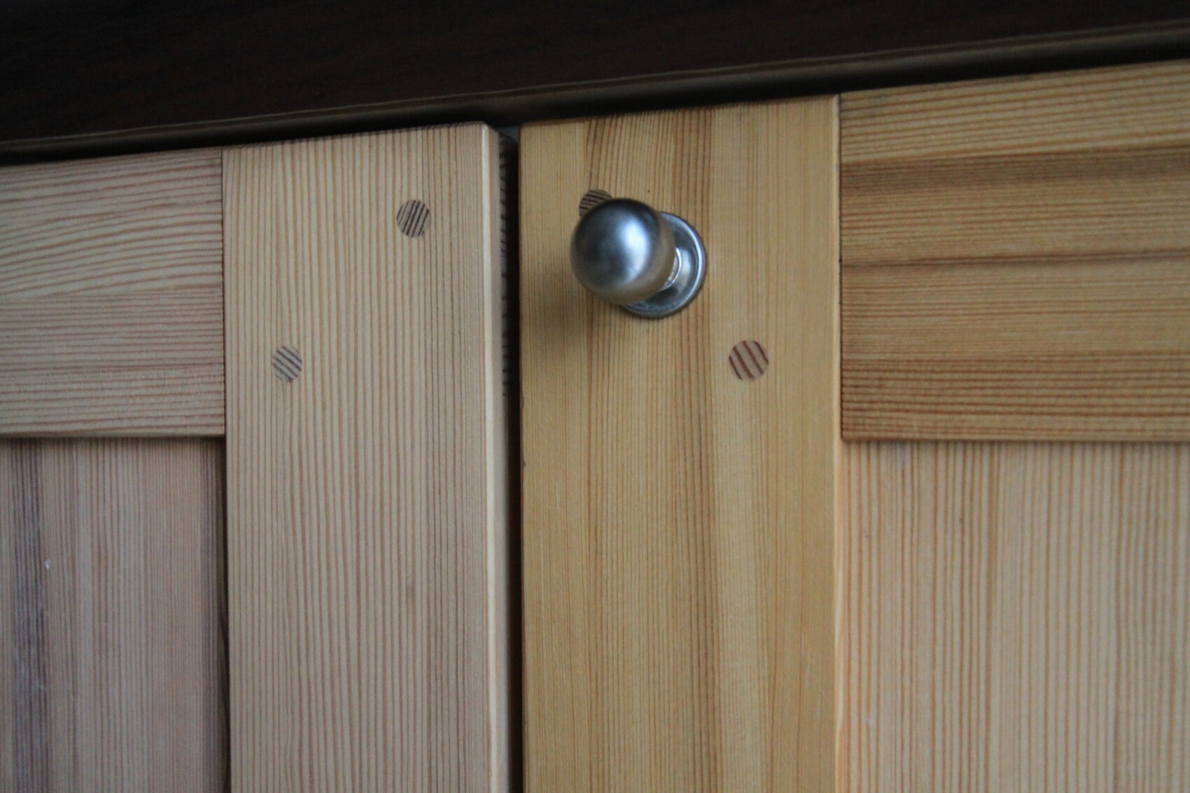 Nahaufnahme von Holzschranktueren mit rundem Metallknauf, Holzmaserung sichtbar