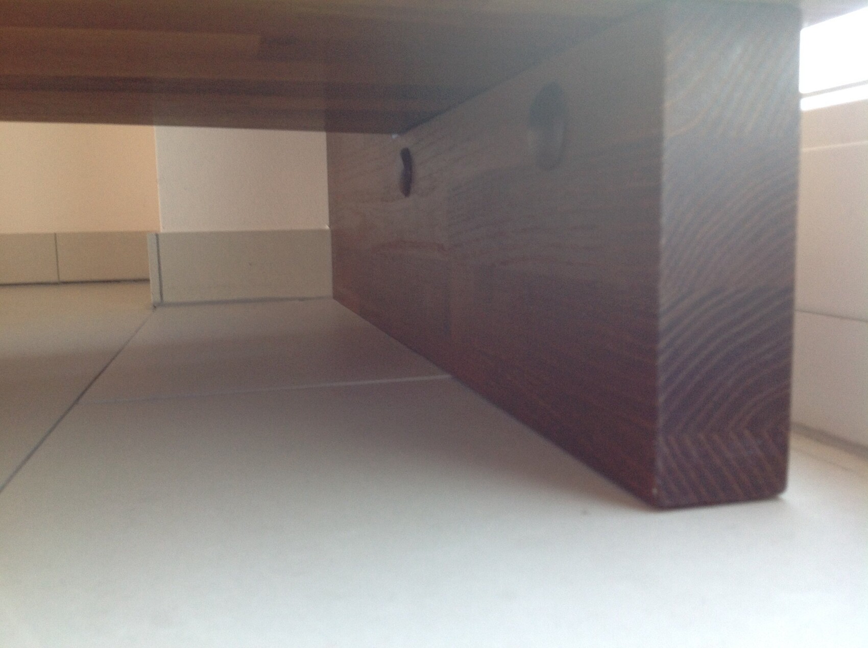 Unterseite eines dunklen Holztischbeins über hellem Fliesenboden