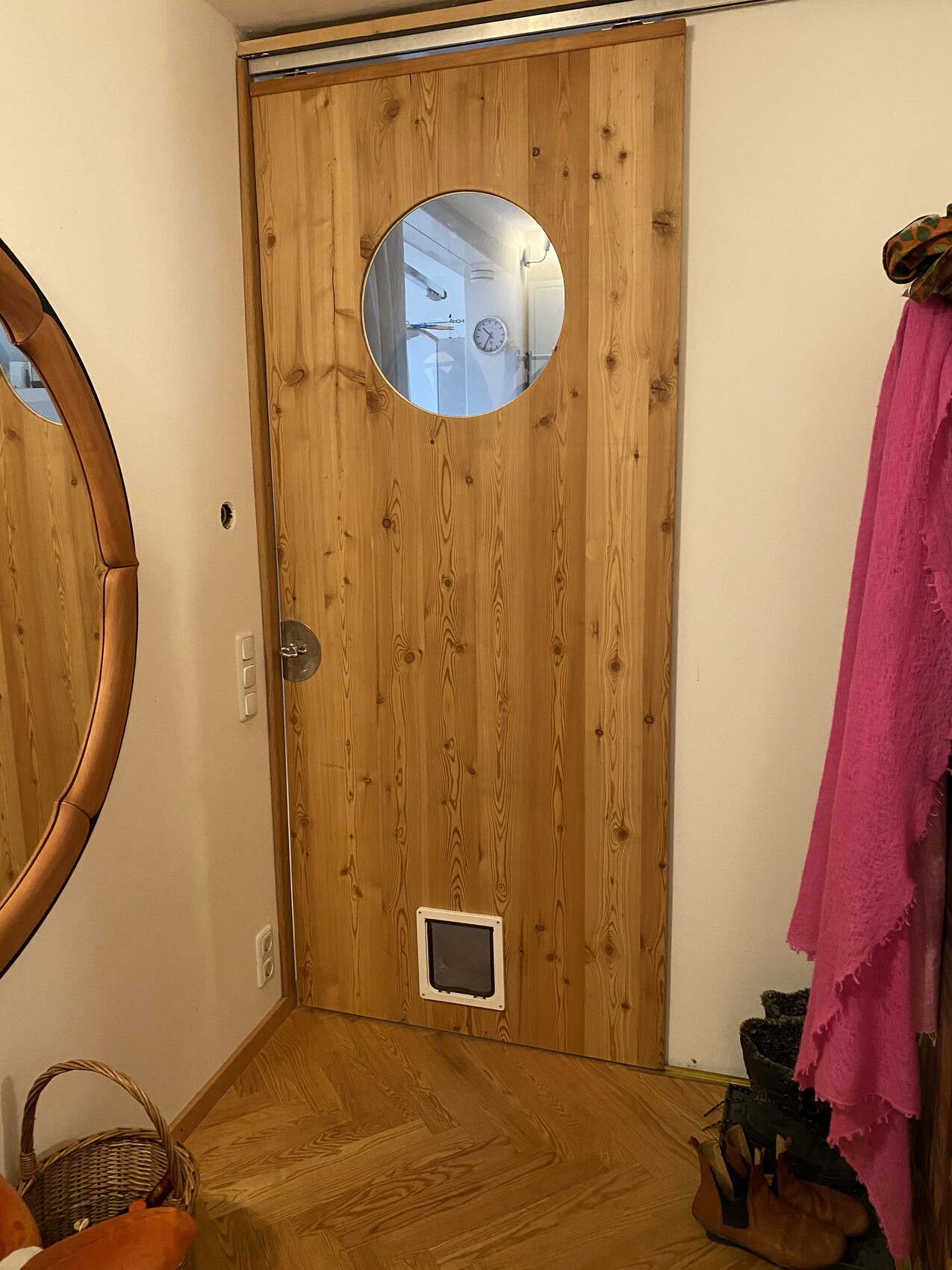 Holztür im Flur mit rundem Fenster, Katzenklappe unten, Spiegel daneben.