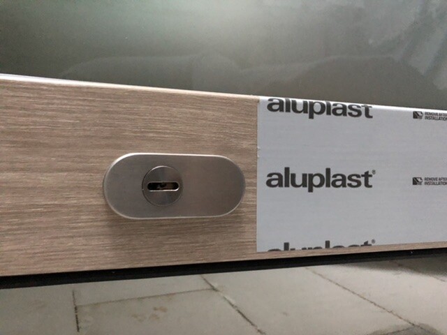 Ovales Metall-Schloss auf Holzplatte; aluplast-Band im Hintergrund.