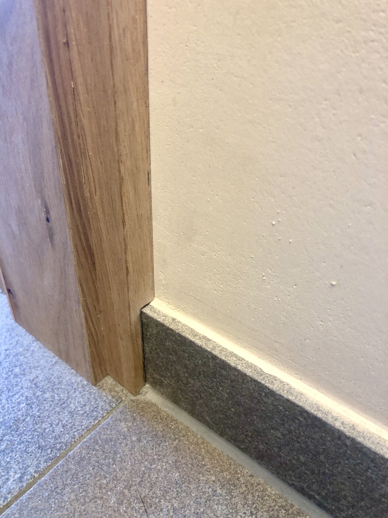 Nahe der Tür: Holzrahmen trifft weiße Wand, graue Sockelleiste und Fliesenboden.