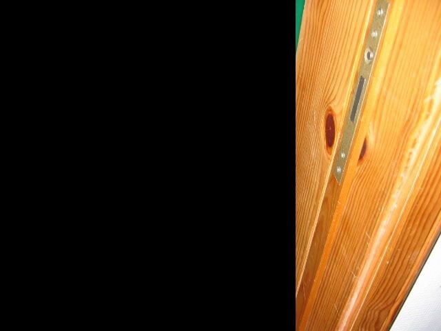 Nahaufnahme eines Holz-Türrahmens mit Metallbeschlag und Schrauben