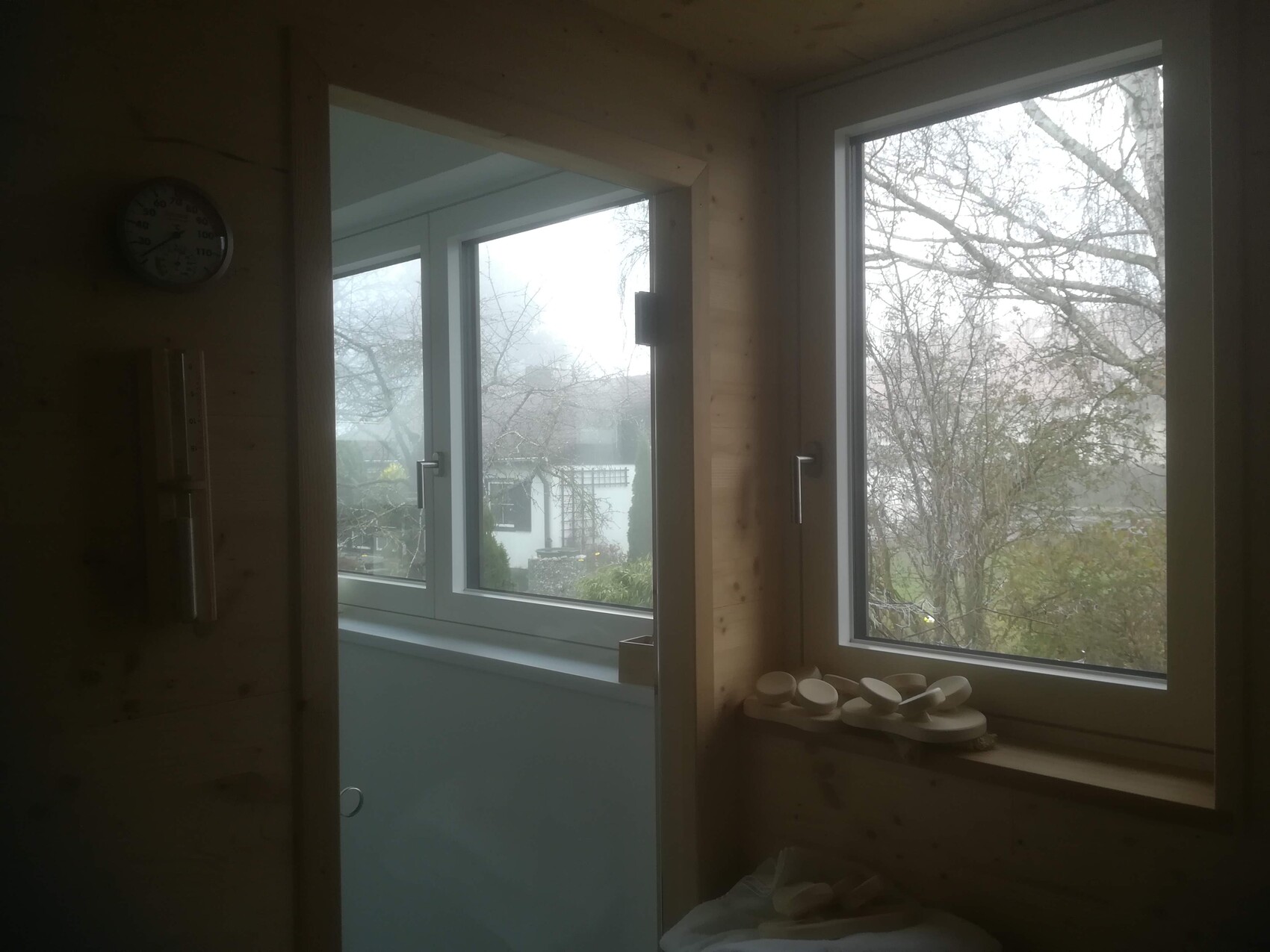 Holzraum mit Blick durch Fenster; Thermometer an der Wand, weiße runde Gegenstände auf Fensterbank