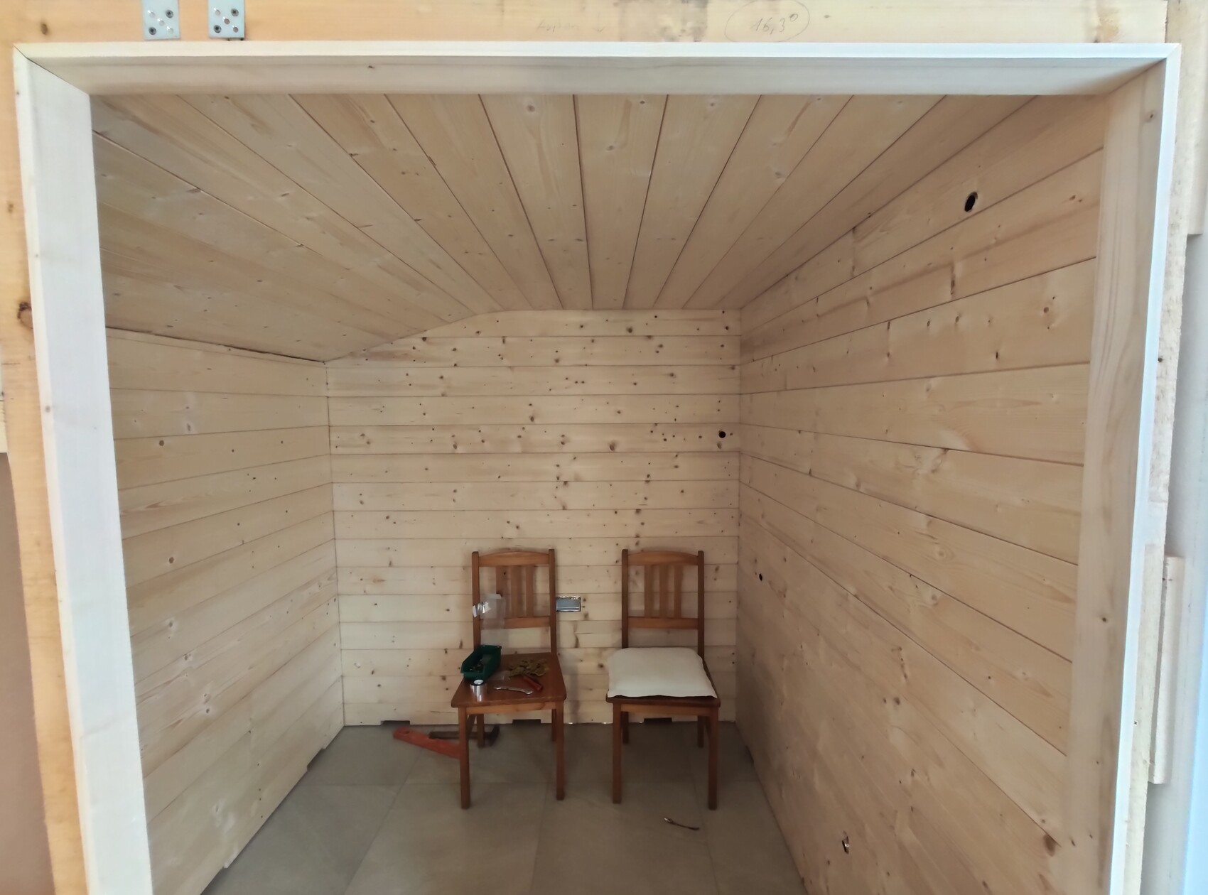 Helleres Holzzimmer mit Paneelwänden und Decke; zwei Holzstühle, Tisch mit Werkzeug.