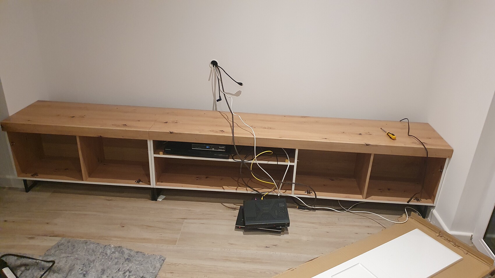 Lange Holzkonsole mit offenen Fächern; Kabelsalat, Wanddose freigelegt, Elektronik unten.
