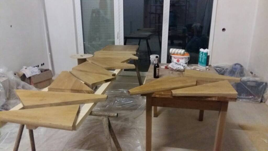 Werkstatt mit Dreiecks-Holzstuecken auf Tischen; Farben und Werkzeuge liegen bereit.