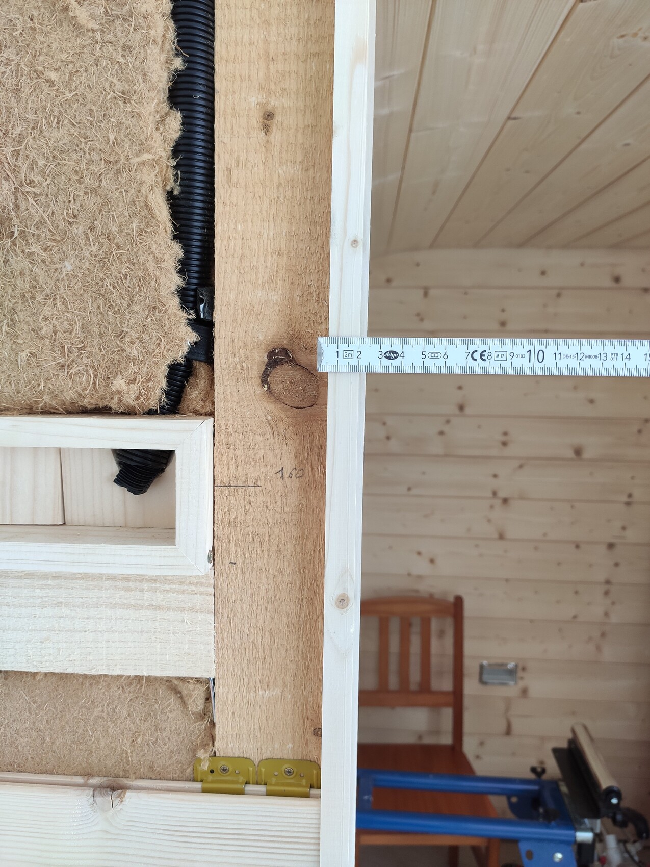 Innenansicht einer Holzkonstruktion mit Dämmung, Kabelkanal, Türrahmen und Messband.