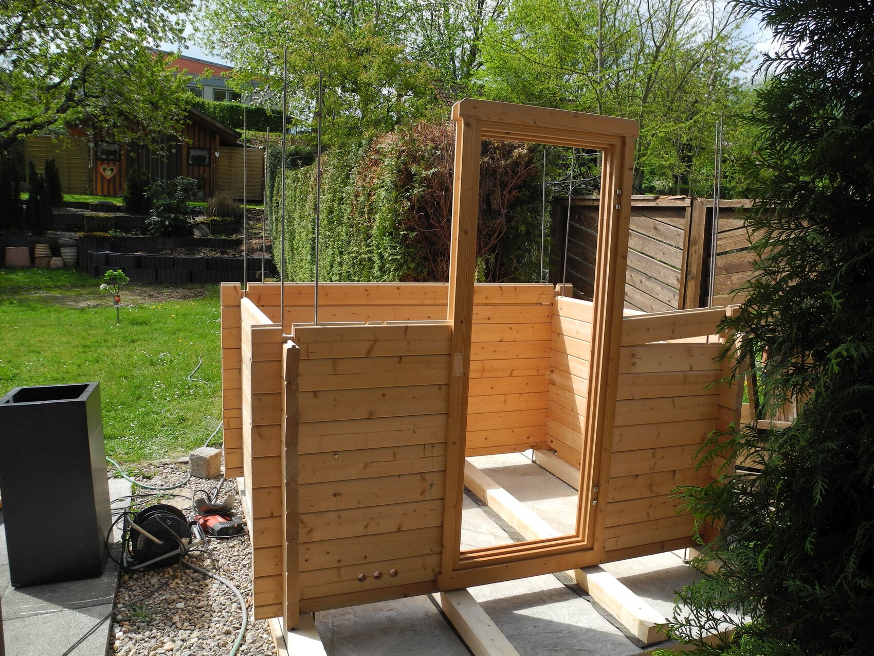 Frisch aufgebaute Holzwand-Konstruktion mit Türrahmen im Garten, Zaun im Hintergrund.