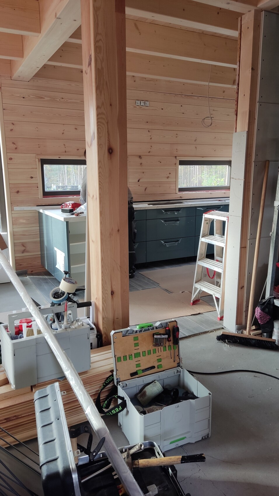 Innenraum eines Holzhauses im Bau: Holzwände, Stützbalken, Küche und Werkzeuge.