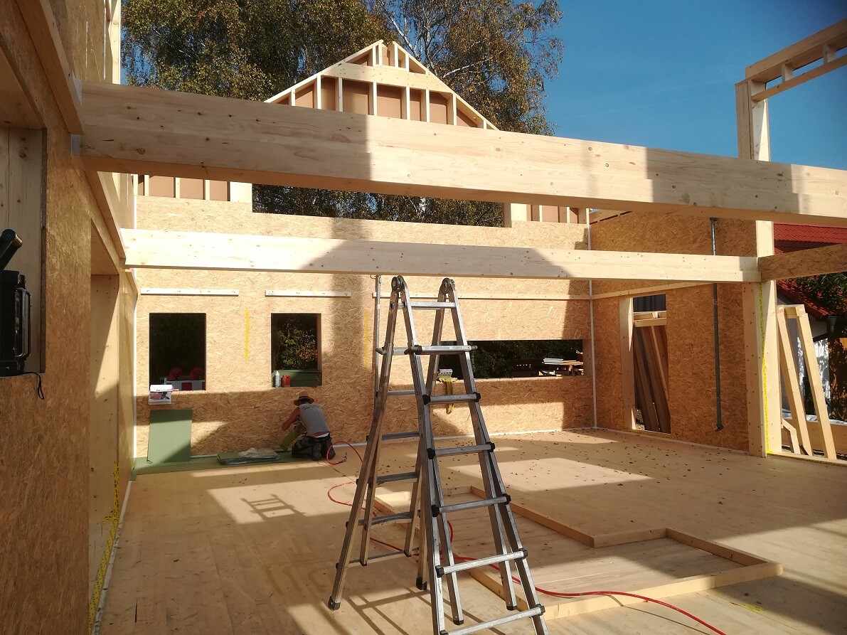 Holzhaus-Rohbau mit Holzrahmen, Bauarbeiter, Leiter und Bauteile im Innenraum