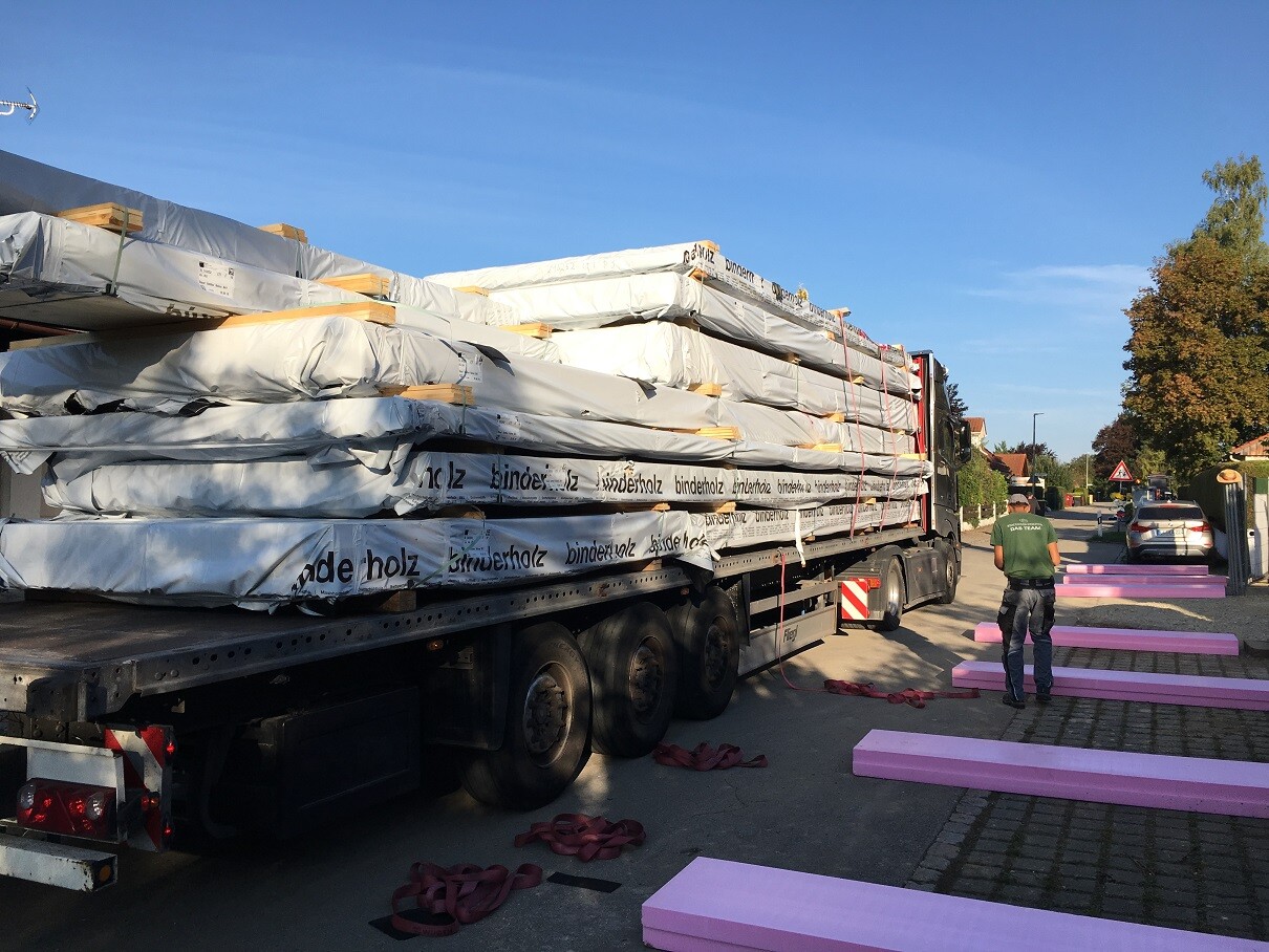 Lastwagen mit beladenem Holzbaustoff-Lieferung; große Holzpakete, pinke Dämmplatten am Straßenrand