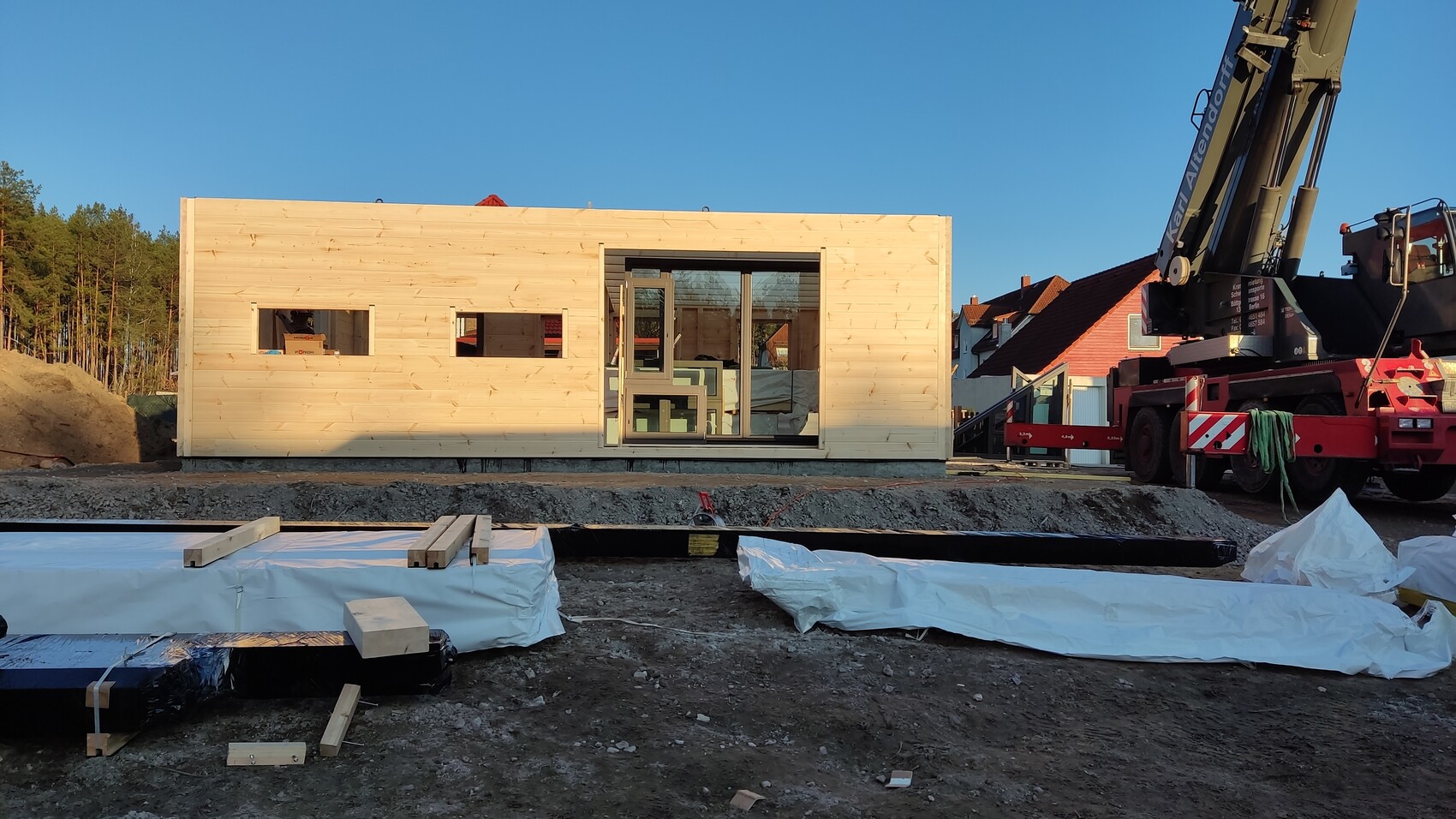 Modulares Holzhaus auf Baustelle mit Kran, Glasfront und Holzverkleidung.