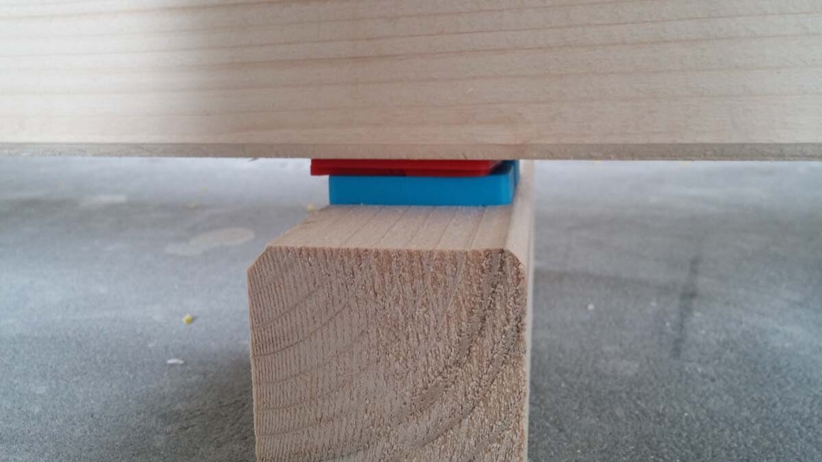 Holzbalken liegt auf einem Holzstumpf, blaue und rote Kunststoffblöcke dienen als Abstandhalter