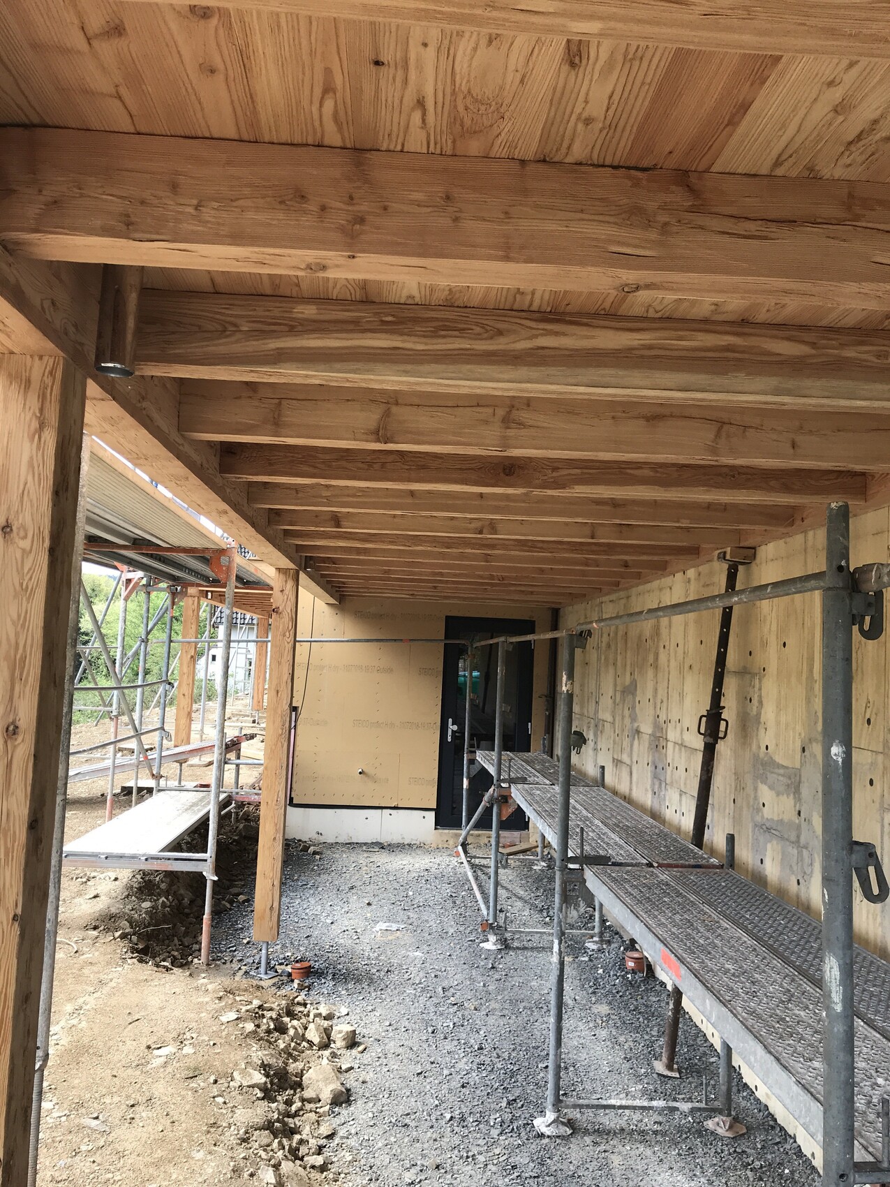 Baustellenaufnahme: Holzbalkendecke, Gerüst, Türöffnung am Gebäude, Kiesboden.
